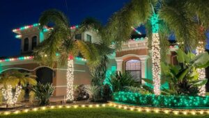 1 Christmas Light Installation in Naples FL 02 Festive home exterior with Christmas lights in Fort Myers FL. Palm trees wrapped in white lights, green lights outlining landscaping, and red and green lights on the roof create a warm holiday glow.