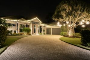 christmas light installation near you in naples fl 47 Night view of a luxurious home decorated with warm white Christmas lights along the roofline and on a large tree in the front yard, illuminating the brick driveway.